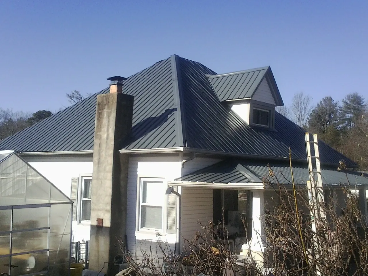 Dark blue standing seam metal roof on a white farmhouse with dormer — Slate & Tile Roof Repair by Roofing Brothers in Phippsburg
