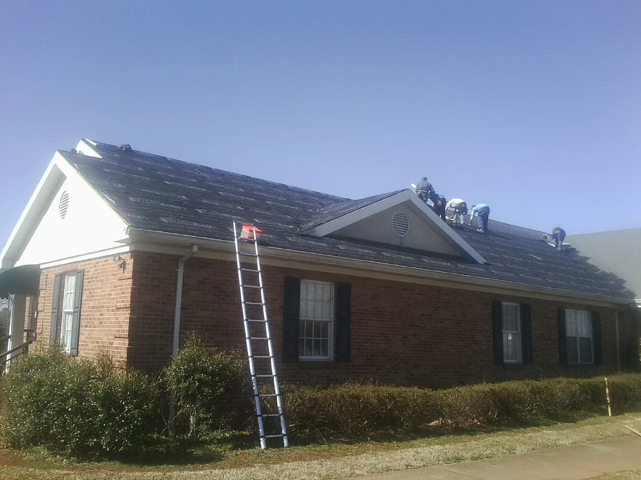 Crew tearing shingles off a brick ranch roof with a ladder set — Emergency Roof Repair work by our crew in Phippsburg