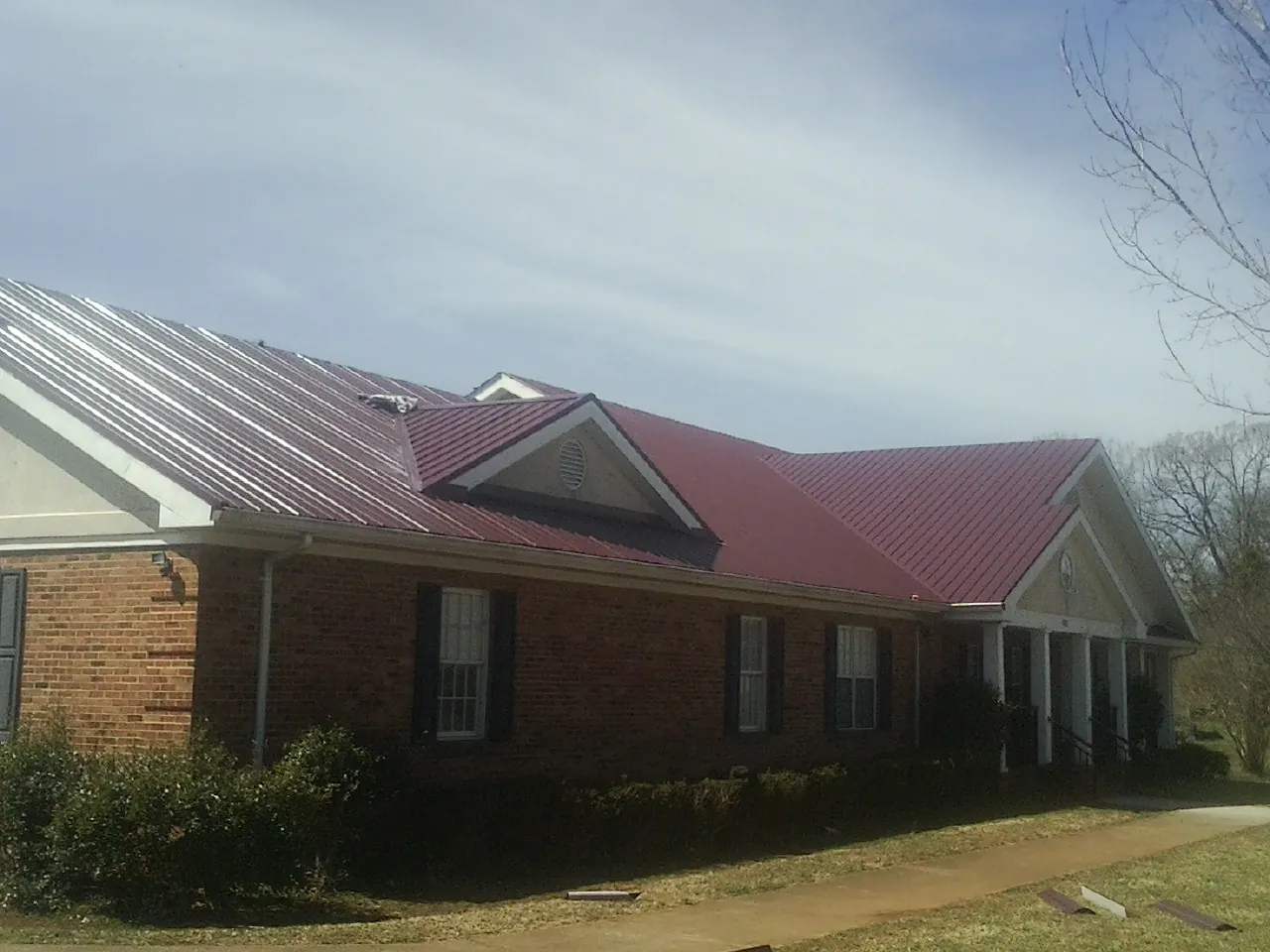 Red metal roof with gabled entries on a long brick building, from a Hail Damage Roof Repair job in Phippsburg