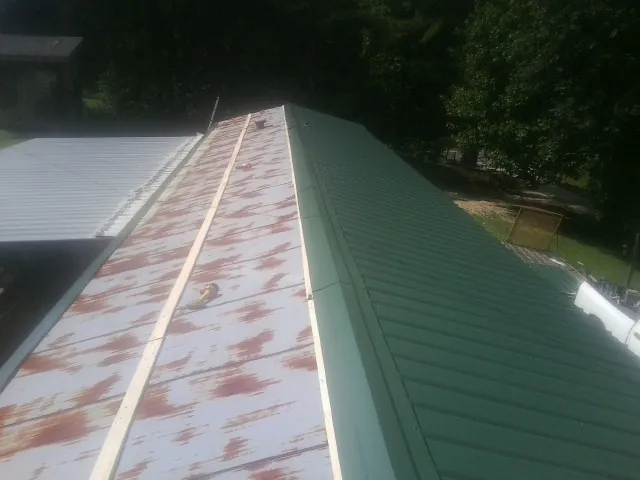 Old rusted panels beside newly installed green metal roofing — Wind Damage Roof Repair by Roofing Brothers in Phippsburg