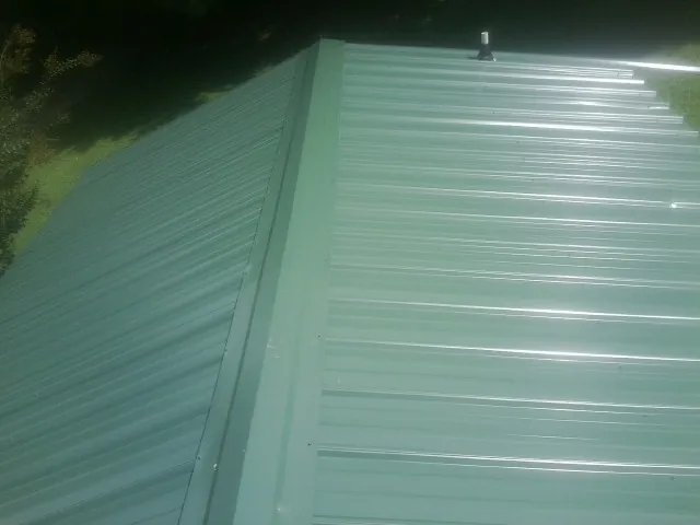 New green metal panels meeting at the ridge of a roof — Flat Roof Repair work by our crew in Phippsburg