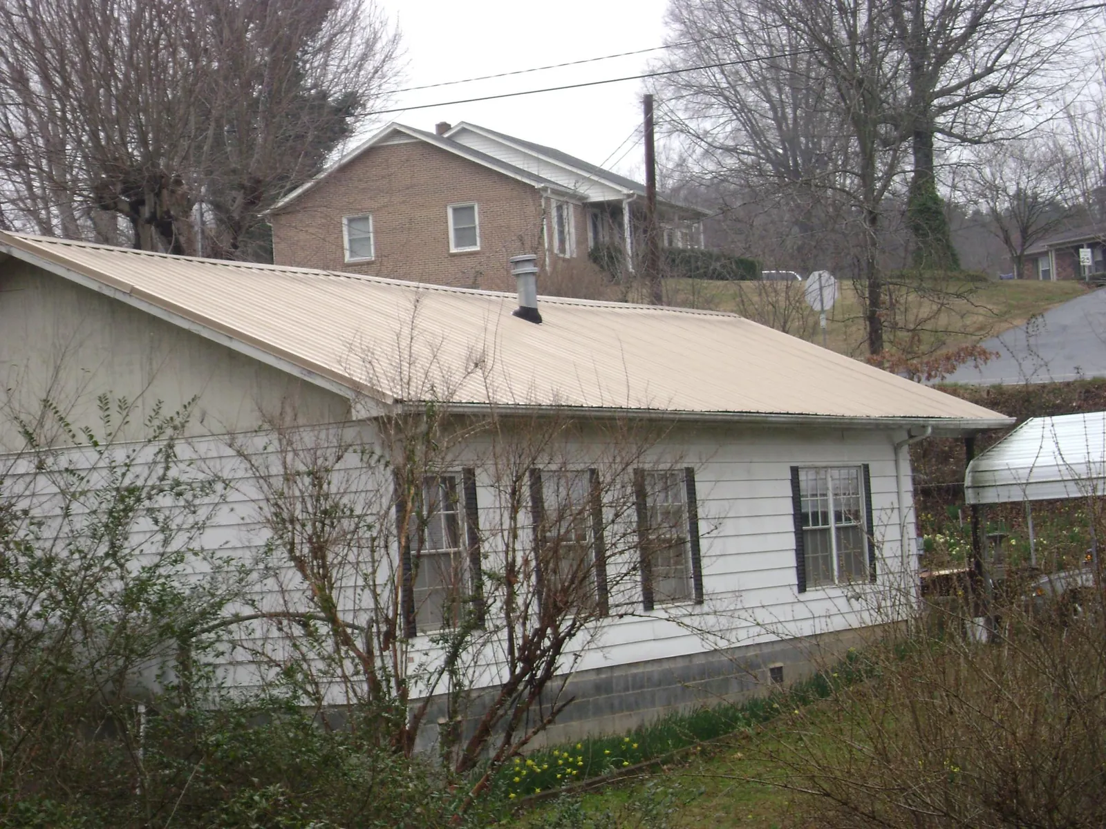 Tan metal roof on a white sided house set into a hillside — Commercial Roofing by Roofing Brothers in Phippsburg