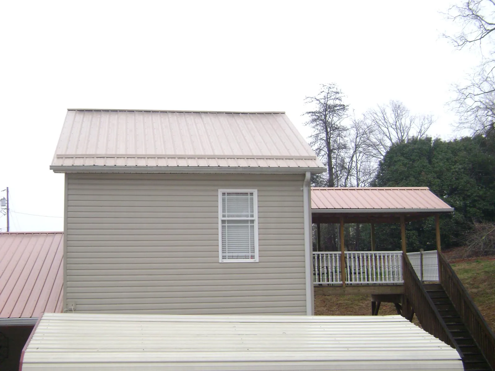 Tan metal roofs on a two story addition and attached porch, from a Roof Replacement job in Phippsburg